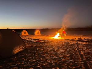 a person standing next to a bonfire on a beach with tents at مخيم همسات الصحراء in Siwa