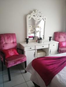 a bedroom with a vanity with a mirror and pink chairs at Iris Bnb on Vaal in Vanderbijlpark
