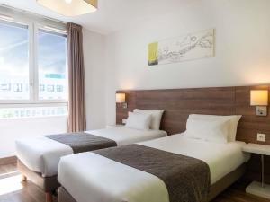 two beds in a hotel room with a window at Adagio Access Grenoble Université in Saint-Martin-dʼHères
