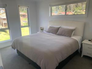 a white bed in a bedroom with two windows at Kuruwa in Tathra