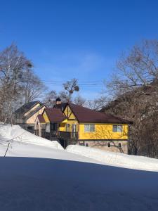 a yellow house with snow in front of it at Corduroy Ski Lodge Madarao Tangram in Shinano