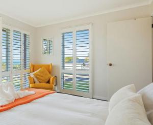 a bedroom with a bed and a chair and windows at Whale Stay in Tathra