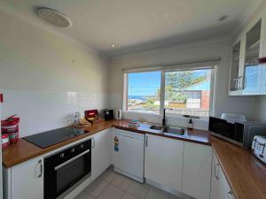 a kitchen with white cabinets and a large window at Whale Stay in Tathra +17 photos