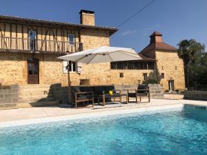 a table with an umbrella next to a swimming pool at Gîte La Carole 120m2 in Monlezun