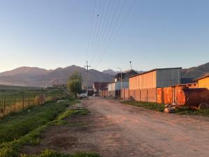 a dirt road with a fence and mountains in the background at Sunrise Panorama in Bokonbayevo