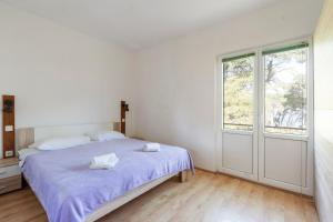a white bedroom with a bed and a window at Apartman Viola 1 in Ugljan