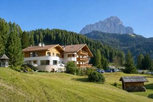 a large house on a hill with mountains in the background at Garni Hotel Rosengarten B&B in Selva di Val Gardena