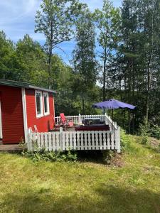 a small red house with a white fence and an umbrella at hytte ved innsjø in Skien