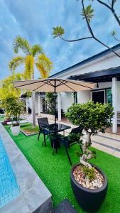 a patio with a table and umbrella and grass at Villa Abadi Resort VAR in Pantai Kok