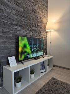 a television on a white tv stand in a room with a brick wall at Studio Apartman 47A in Valjevo
