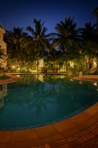 a swimming pool with palm trees at night at Riviera Hermitage in Arpora