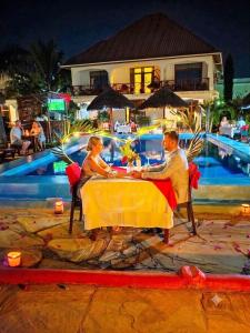 a man and woman sitting at a table by a pool at Mimi na wewe villa in Nungwi