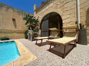 a patio with a pool and two chairs next to a building at A la maison B&B in Xagħra