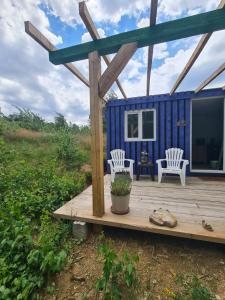 a blue tiny house with two white chairs on a wooden deck at Purple Diamond in Damiş