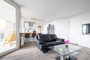 a living room with a black leather couch and a glass table at Komfortable Ferienwohnung für 2 am Südstrand mit Wintergarten & Meerblick Wohnung 12 in Wilhelmshaven