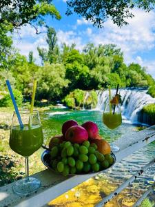a plate of fruit and two glasses of wine next to a waterfall at Villa Koćuša in Ljubuški