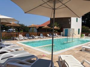 a swimming pool with lounge chairs and an umbrella at Mobil-home proche plage in Saint-Julien-en-Born