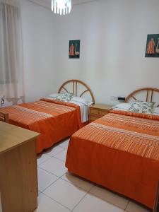 three beds with orange sheets in a room at Hostal La Madrileña in La Gudiña