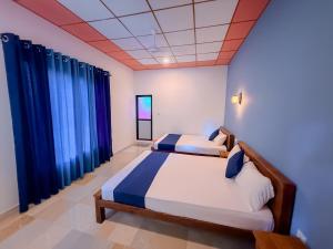 a bedroom with two beds and blue curtains at Deer Inn - Yala in Tissamaharama +30 photos