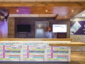 a woman is standing behind a counter with a screen at ibis budget Marseille Aeroport Provence in Marignane