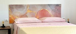 a bed with two pink pillows and a painting on the wall at La Zia Acida Apartment in Ca Tiepolo