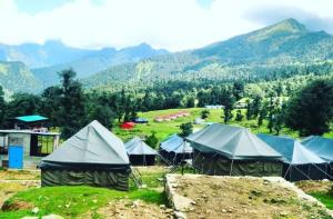 a group of tents in a field with mountains in the background at Chaukhamba Camp Stay in Chopta