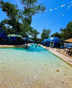 a swimming pool with blue tents and people in the water at Hotel Glamping Horizonte Maya in Chetumal