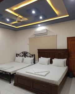 two beds in a room with a ceiling at Nursery Lodge Guest House in Karachi
