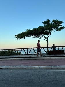 two people walking past a bench and a tree at Refúgio ensolarado a poucos passos do mar in Navegantes