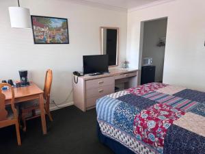 a hotel room with a bed and a desk with a television at Golden West Motel in Klamath Falls +18 photos