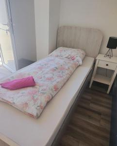 a bed with a pink comforter and a side table at Porto Apartmani in Zvornik