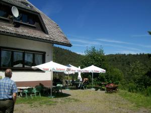 a man walking past a building with tables and umbrellas at Berggasthaus Präger Böden in Todtnau
