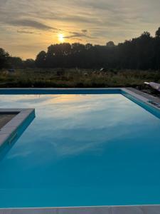 a large blue swimming pool with the sunset in the background at Les nids de la chevêche in Saint-Pierre-de-Juillers