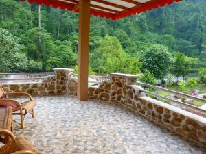 a porch with a stone wall and chairs and trees at Riverside Guesthouse in Bukit Lawang