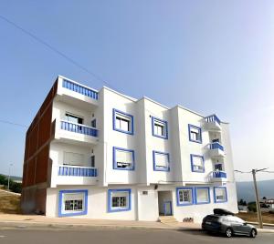 a white building with blue windows and a car at Dalal house in Chefchaouen