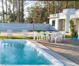 a pool with white chairs and a table and a volleyball court at Morada dos eucaliptos in Capão da Canoa