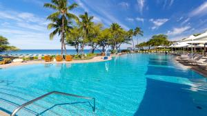 a large swimming pool with palm trees and the ocean at ❤PiH❤ Hapuna Surfside Beachfront Steps From Ocean B26 in Hapuna Beach