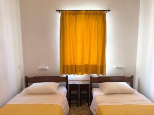 two beds in a room with a yellow curtain at Kythereia Hotel in Agia Pelagia