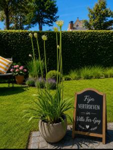 a sign in a garden with a potted plant at VILLA FER-GUY " Beeldige Suite met parking, nabij strand en casino" in Knokke-Heist