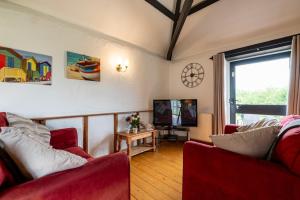 a living room with two red chairs and a television at Braddon - Treworgie Barton Cottages in Bude