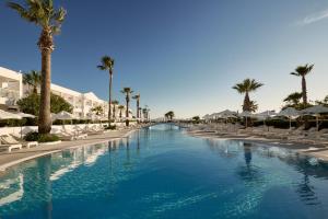 a large swimming pool with chairs and palm trees at Sandy Beach Resort by Rizos Resorts in Agios Georgios