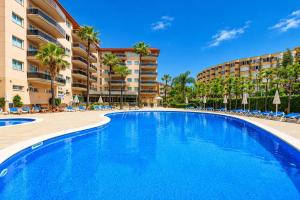 a swimming pool in a resort with chairs and palm trees at Rentalmar Pineda Suites in La Pineda