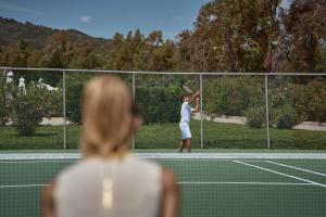 a woman watching a tennis player on a court at Sandy Beach Resort by Rizos Resorts in Agios Georgios