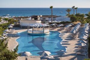 a swimming pool with umbrellas and chairs and the ocean at Sandy Beach Resort by Rizos Resorts in Agios Georgios
