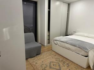 a white bedroom with a bed and a chair at MiraReal Guest House in Macieira da Lixa