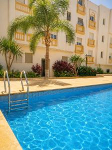 a swimming pool in front of a building with a palm tree at Appartement cosy à 5 min de la plage Sidi Kacem in Hajreien