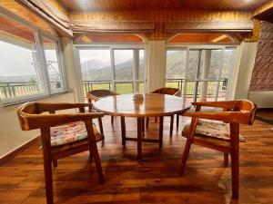 a dining room with a table and chairs and windows at Dhauladhar Vista in Pālampur