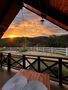 a view of a sunset from a porch with a wooden table at Chalé Recanto do Quilombo - MV in Camanducaia