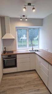 a kitchen with white cabinets and a sink and two windows at Petite Haven in Grobiņa