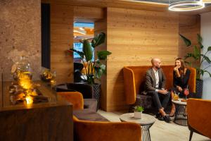 a man and woman sitting on orange chairs in a lobby at Hotel Paganella Andalo in Andalo